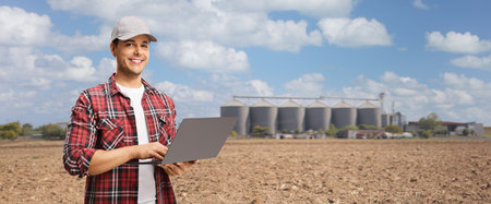 Farmer holding a laptop computer on a field with agricultural silos towersの写真素材