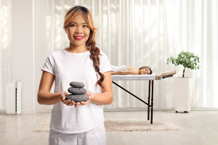 Asian massage therapist holding massage stones in a room with a female clientの写真素材