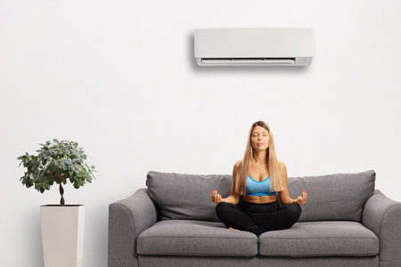 Young woman meditating on a couch under an air conditioning unitの写真素材