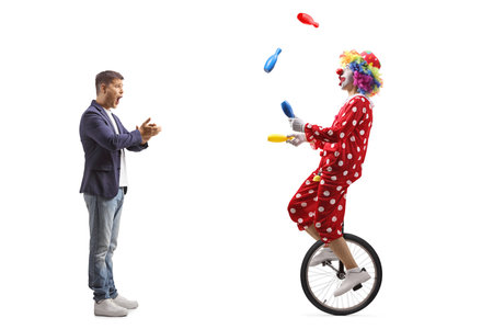 Amazed man clapping and watching a clown juggling on a mono cycle isolated on white backgroundの写真素材