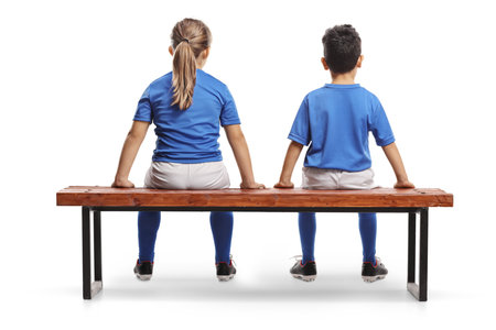 Rear view shot of children sitting on a bench at football training isolated on white backgroundの写真素材