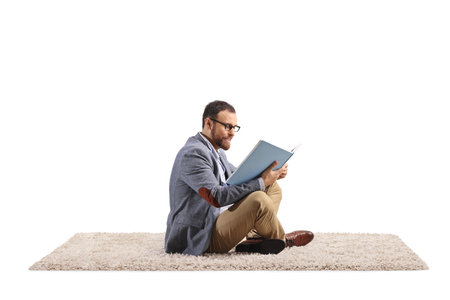Man sitting on a carpet and reading a book isolated on white backgroundの写真素材