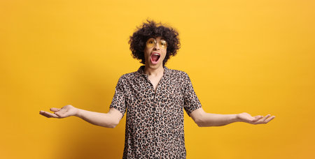 Young man with curly hair and an animal print shirt against yellow backgroundの写真素材