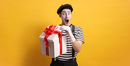 Mime opening a gift box against a yellow backgroundの写真素材