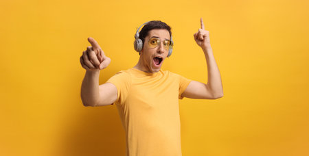 Young man listening to music and dancing against yellow background