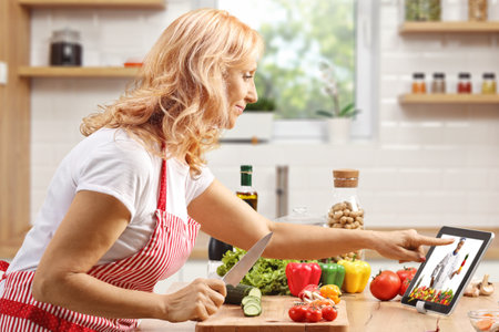 Mature woman cooking and watching a video on a digital tabletの写真素材