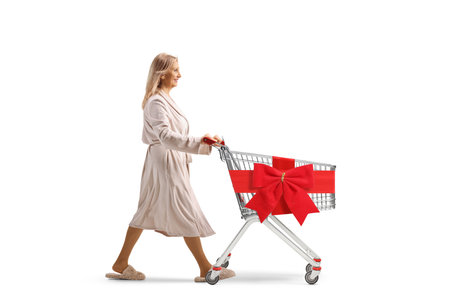 Woman in a bathrobe pushing a shopping cart with red ribbon bow isolated on white backgroundの写真素材