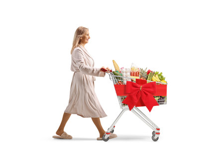 Woman in a bathrobe pushing a shopping cart with red ribbon bow and food isolated on white backgroundの写真素材