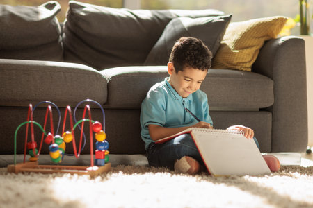 Cute boy sitting on a carpet at home and drawing