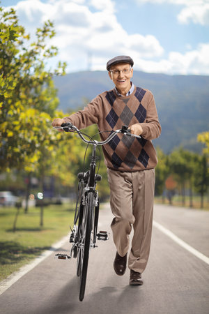 Elderly man pushing a bicycle in a parkの写真素材