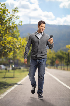 Full length portrait of a young man using a phone and walking in a parkの写真素材