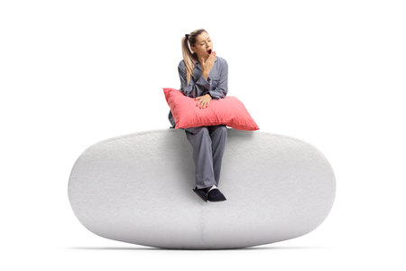 Young woman sitting with a pillow and yawning isolated on white backgroundの写真素材