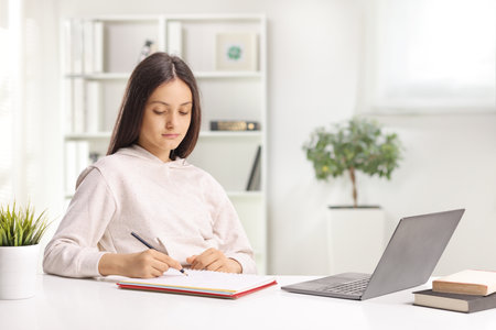 Female student with a laptop writing homeworkの写真素材