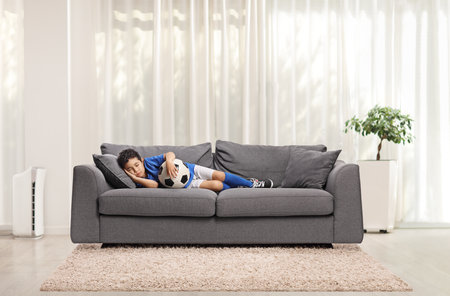 Boy in a football jersey sleeping on a sofa in a living room