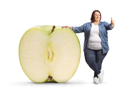 Overweight woman with a big apple gesturing thumbs up isolated on white backgroundの写真素材