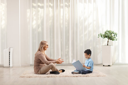 Mother and son sitting on carpet and reading a book at homeの写真素材