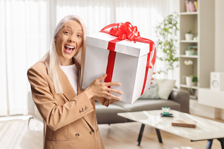Happy woman holding a present box at home in a living roomの写真素材