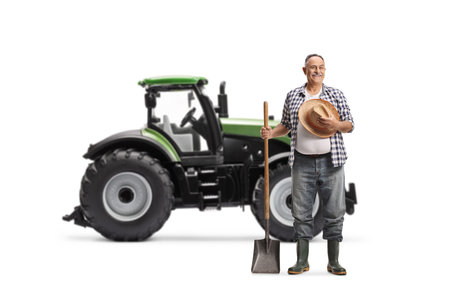 Farmer with a straw hat and a spade standing in front of a tractor isolated on white backgroundの写真素材
