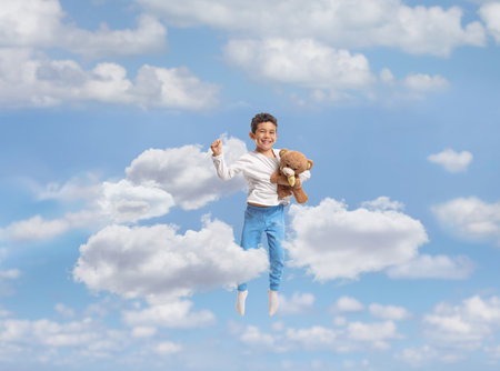 Full length portrait of a boy in pajamas holding a teddy bear and jumping isolated on white backgroundの写真素材