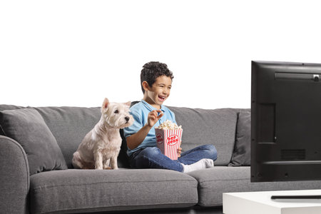 Kid and a dog sitting on a sofa and eating popcorn isolated on white background