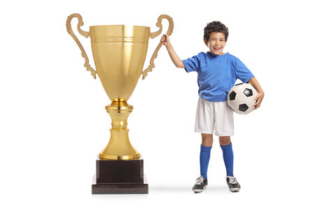 Kid football player with a big gold tropy cup isolated on white backgroundの写真素材