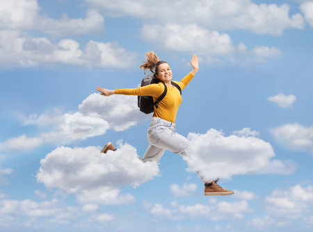 Female student with a backpack jumping high in the skyの写真素材