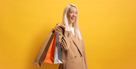 Happy woman carrying shopping bags against a yellow backgroundの写真素材