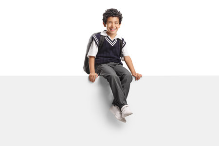 Happy asian schoolboy in a uniform sitting on a white panel isolated on white backgroundの写真素材