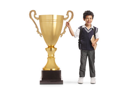Schoolboy in a uniform holding a big trophy cup isolated on white backgroundの写真素材