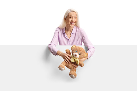 Woman holding a teddy bear behind a white panel isolated on white backgroundの写真素材