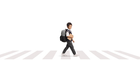 Asian schoolboy in a uniform walking at a zebra crossing and holding a book isolated on white backgroundの写真素材