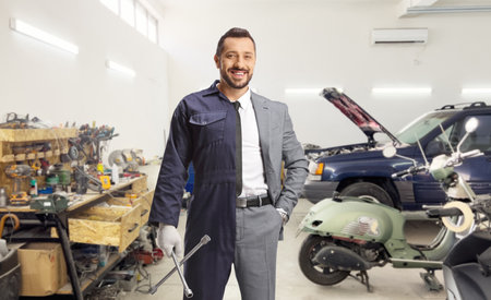 Businessman wearing auto mechanic uniform and holding a wrench at a car garageの写真素材