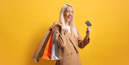 Happy woman with shopping bags and a card against a yellow backgroundの写真素材