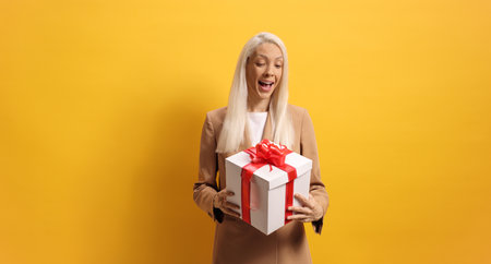 Surprised young woman looking at a present box against yellow backgroundの写真素材