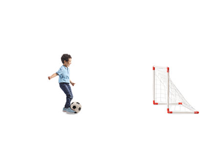 Full length profile shot of an asian boy running with a football and scoring a goal isolated on white backgroundの写真素材