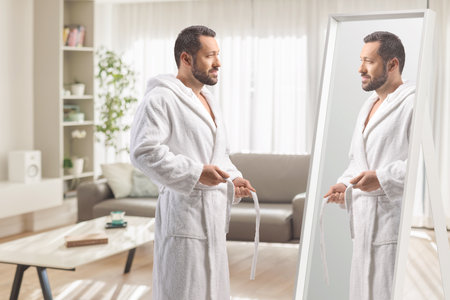 Man putting on a bathrobe in front of a mirror at homeの写真素材
