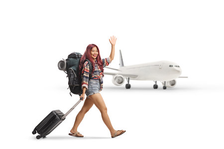 Asian female tourist at the airport walking with a suitcase and waving at camera isolated on white backgroundの写真素材