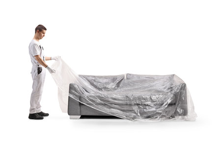 House painter covering a sofa with a plastic drop cloth isolated on white backgroundの写真素材