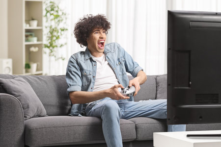 Excited guy sitting on a sofa and playing video games at homeの写真素材