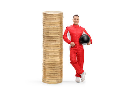 Full length portrait of a car racer in a red suit leaning on a pile of coins isolated on white backgroundの写真素材