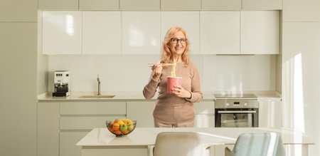 Middle aged woman with a box of noodles in a kitchenの写真素材