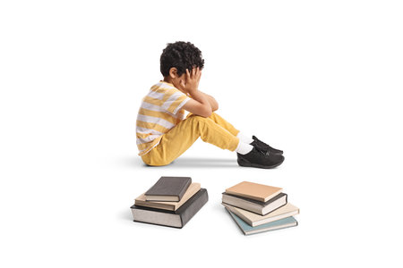 Sad kid sitting on the floor with books isolated on white backgroundの写真素材