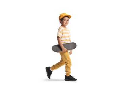 Little boy with a yellow cap walking and carrying a skateboard isolated on white backgroundの写真素材