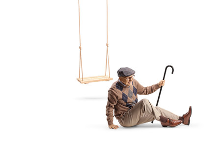 Elderly man with a cane falling from a swing and sitting on the ground in pain isolated on white backgroundの写真素材