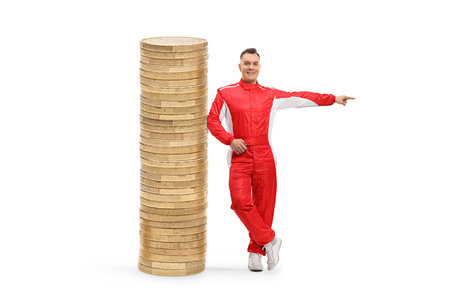 Full length portrait of a car racer leaning on a pile of coins and pointing to the side isolated on white backgroundの写真素材