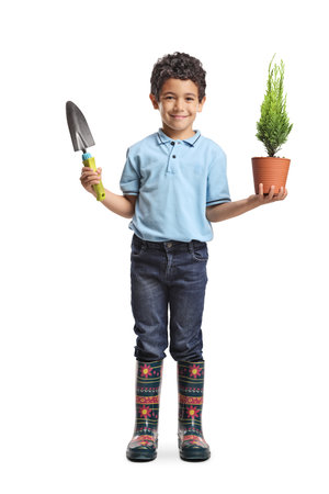 Asian boy holding a small tree in a pot and a spade isolated on white backgroundの写真素材