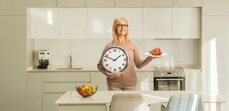 Woman holding cooked meat on a plate and a clock in a kitchenの写真素材