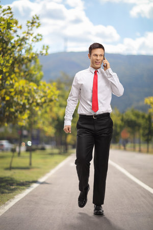 Businessman walking in a park and using a phoneの写真素材