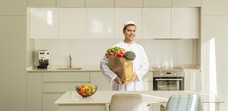 Middle eastern man holding a shopping bag with groceries in a kitchenの写真素材