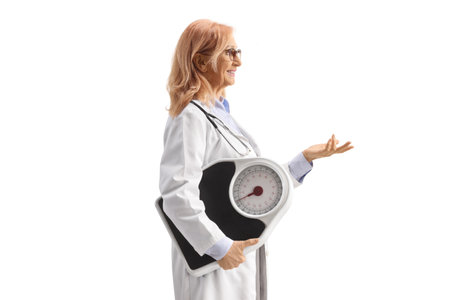 Female doctor holding a weight scale and gesturing with hand isolated on white backgroundの写真素材